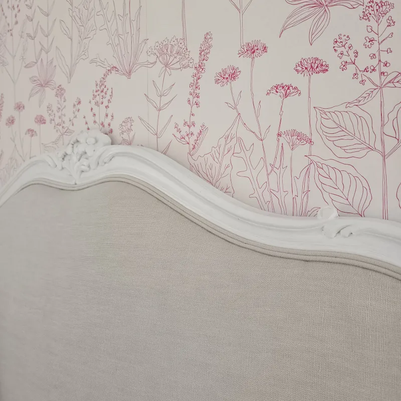 Le papier peint fleuri fait rentrer la nature dans la chambre, avec une tête de lit chinée recouverte d'un lin haut de gamme